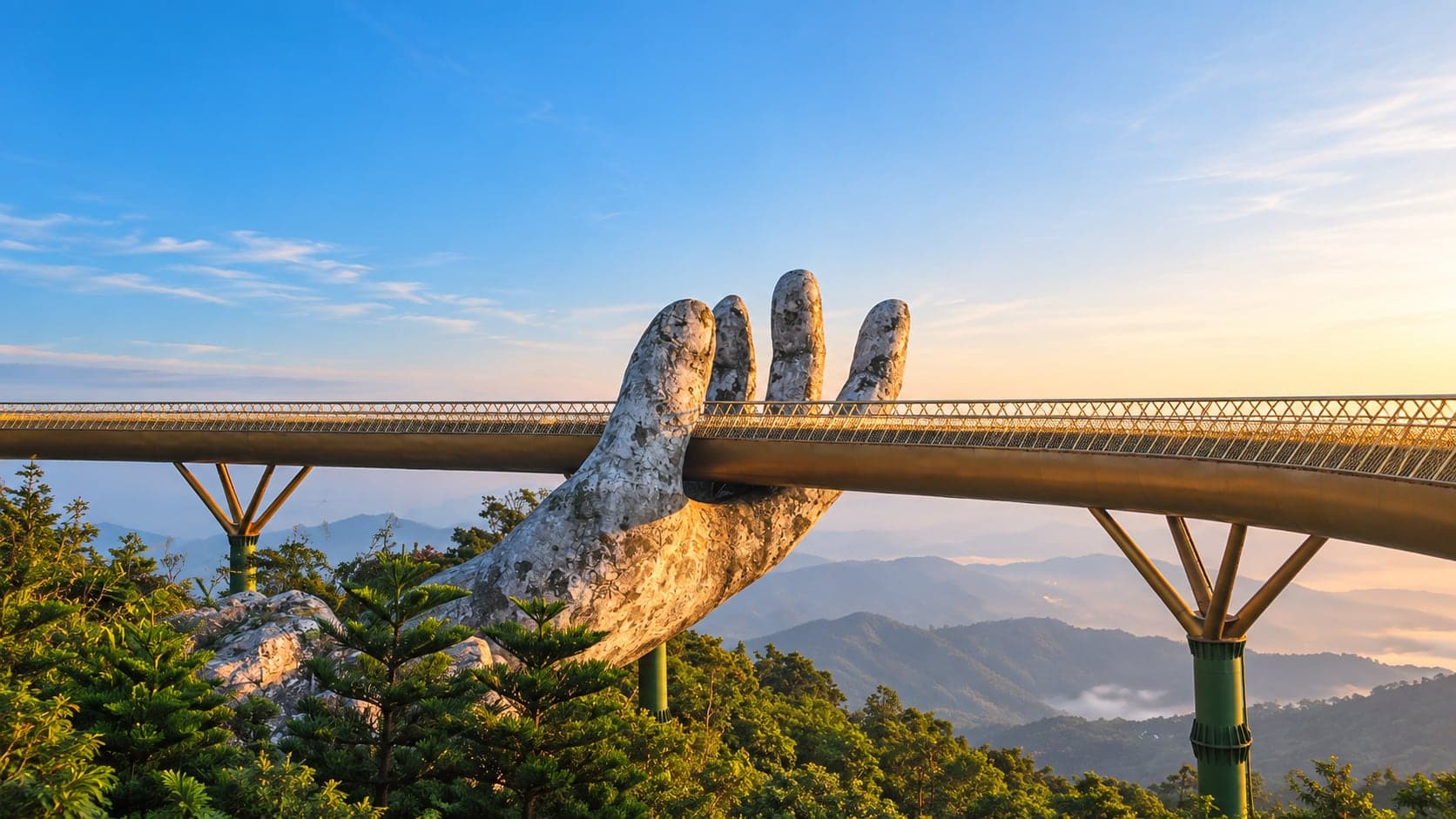 A golden footbridge held up by two giant stone hands above a forested mountain ridge at sunrise.